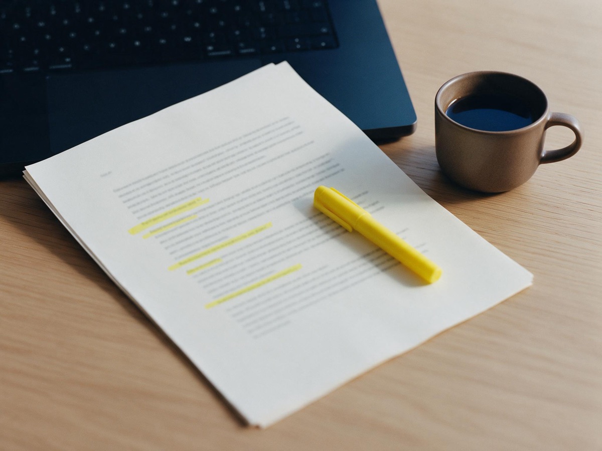 Schriftstück mit gelb markierten Zeilen, Textmarker und Kaffeetasse
